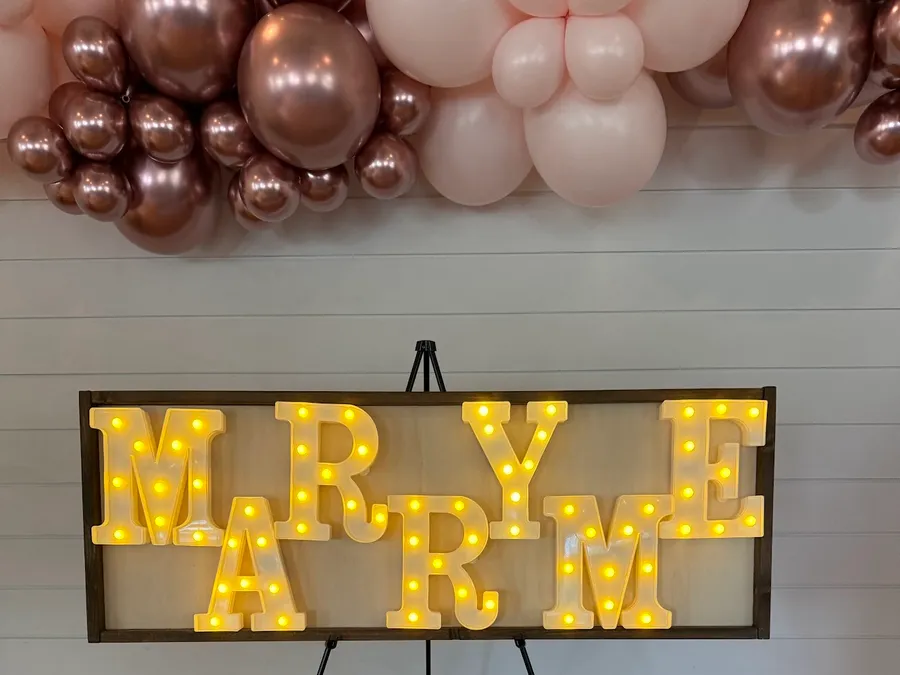 A lit MARRY ME marquee sign beneath a rose-gold and blush organic balloon garland at George Coffee + Provisions in Coppell, TX.