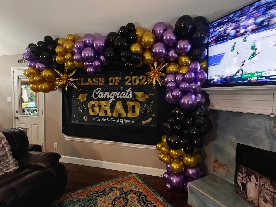 An organic balloon garland in chrome purple, gold, and black with gold foil starbursts framing a Class of 2025 Congrats Grad backdrop, built for a Lamar Jackson themed graduation party in Corinth, TX.