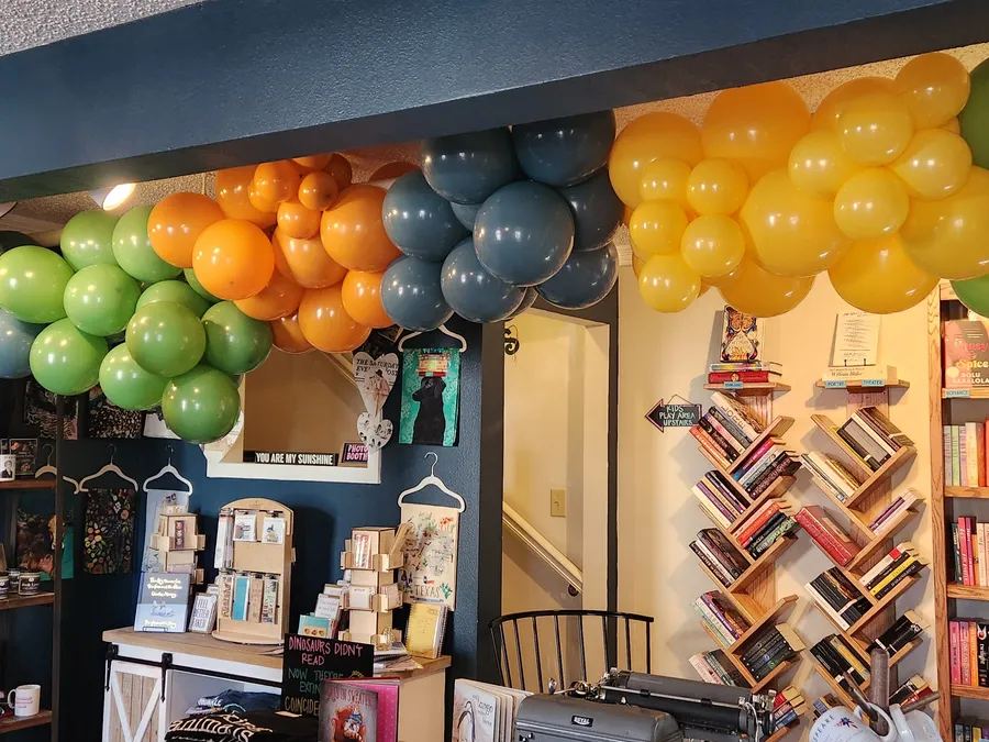 A jungle-themed green, orange, blue, and gold organic balloon garland over the bookshelves at Talking Animals Books in Grapevine, TX.