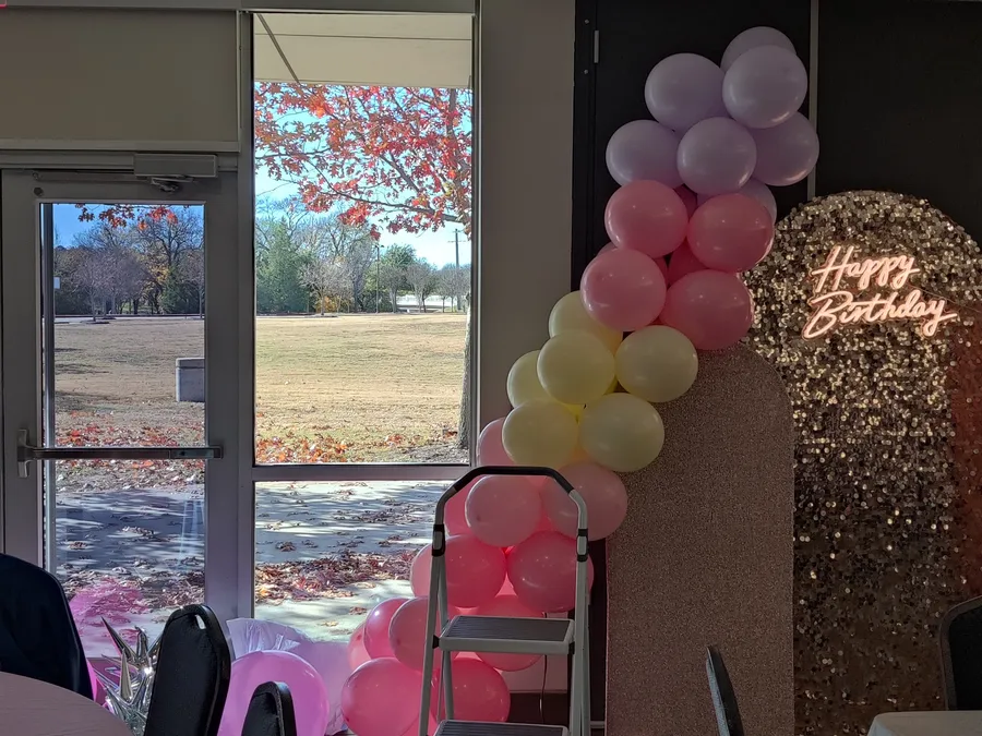 A pastel pink, lavender, mint, and yellow organic balloon garland framing a large analog clock with LED countdown displays, a silver disco ball, and silver starbursts, a Taylor Swift Midnights-themed birthday backdrop at The Keller Pointe in Keller, TX.